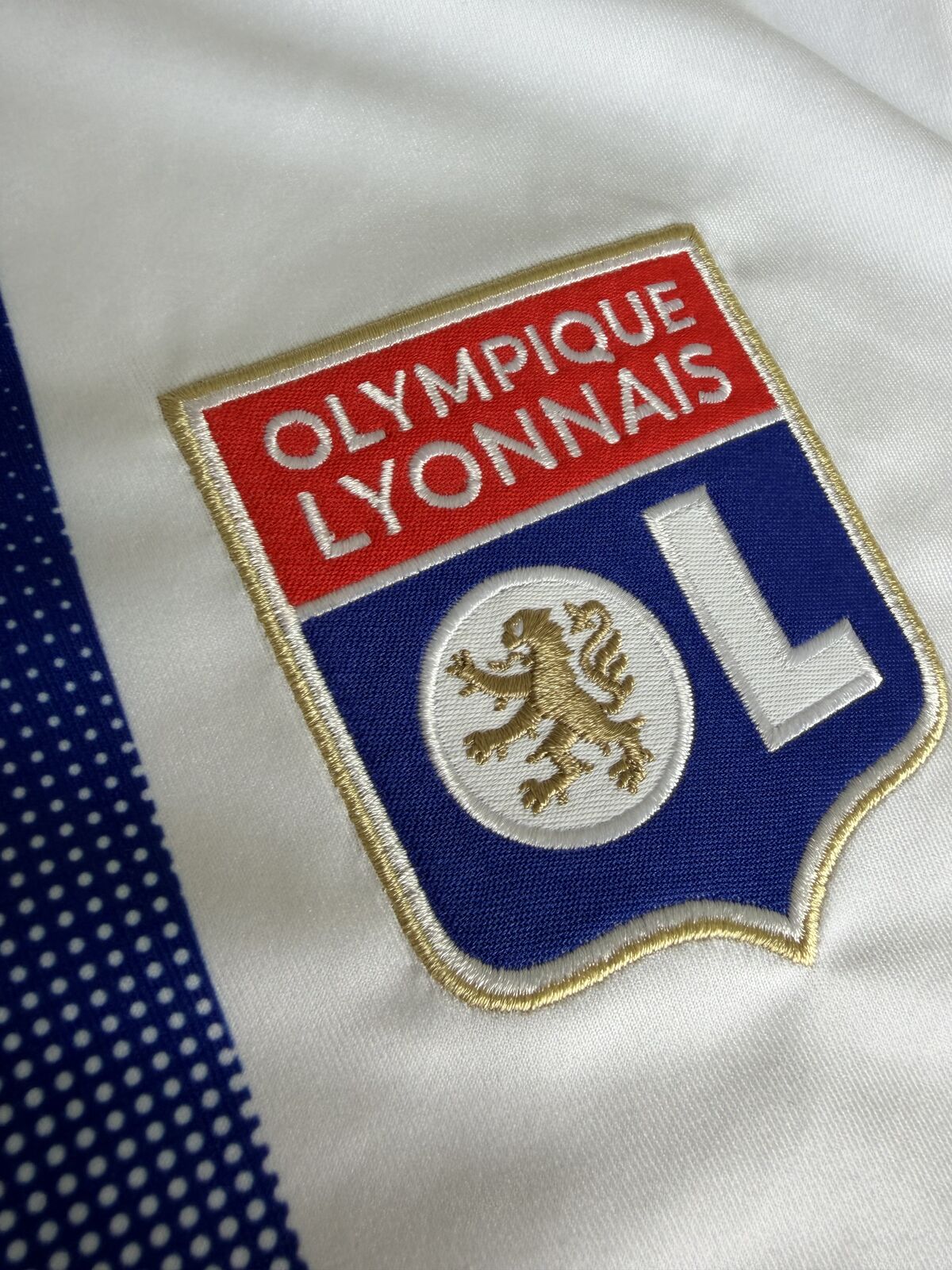 Close-up of the embroidered Olympique Lyonnais crest showing the gold lion, red and blue fields and gold border