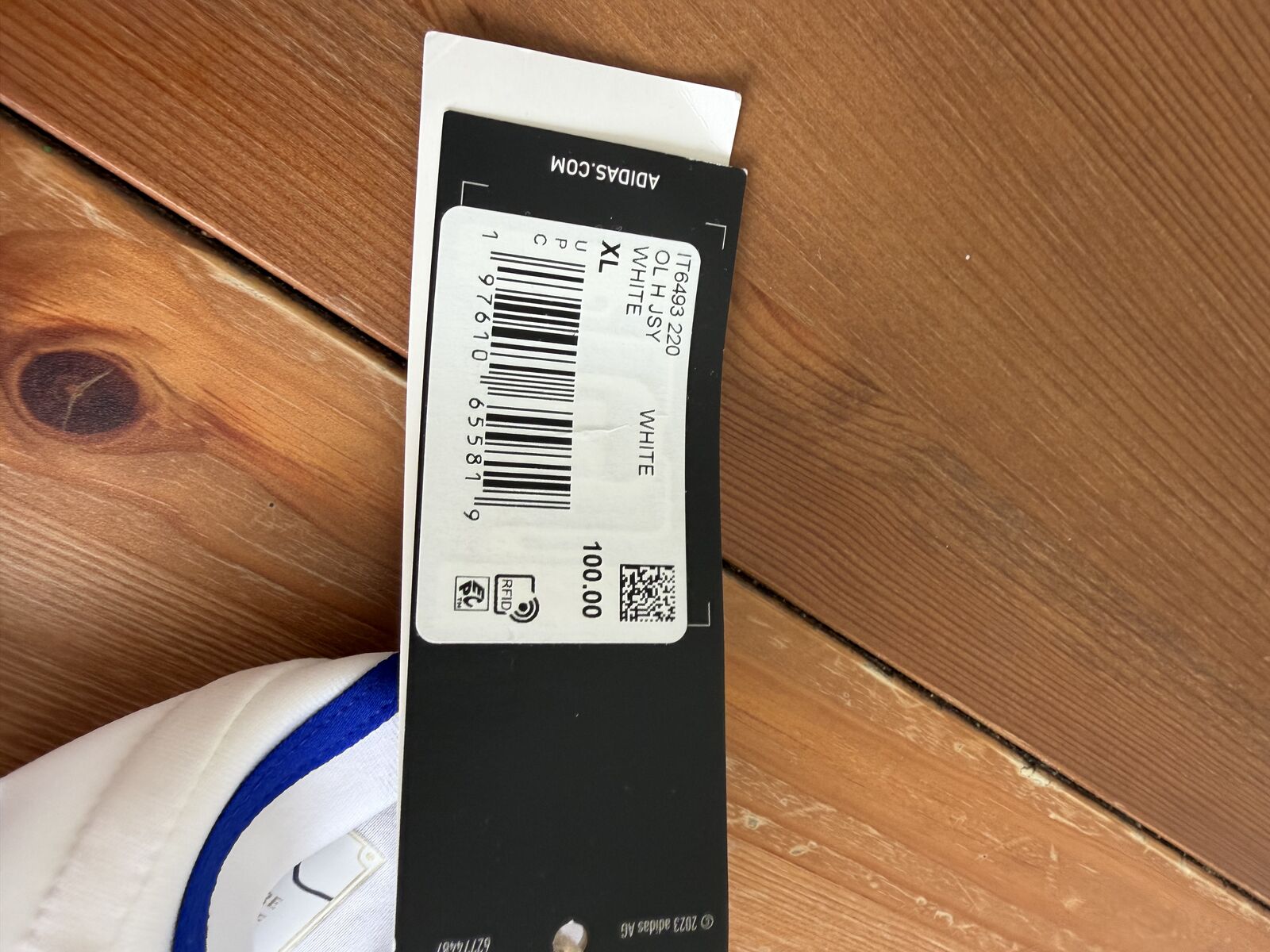Cardboard hangtag printed with IT6493 220, OL H JSY, WHITE, XL, price 100.00, a barcode, QR code, RFID symbol and adidas.com
